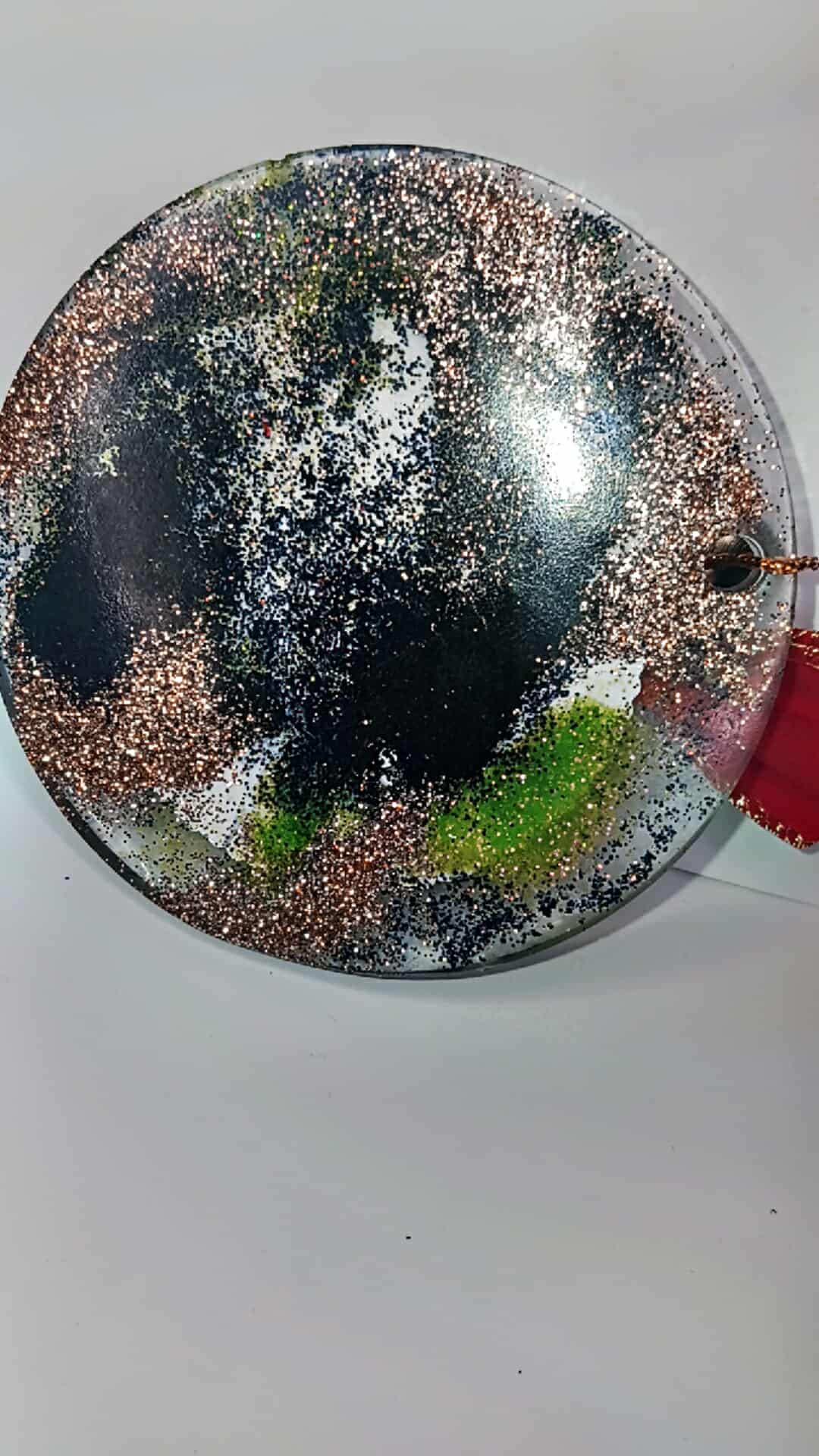 Round decorative item with metallic and green speckles on a white background