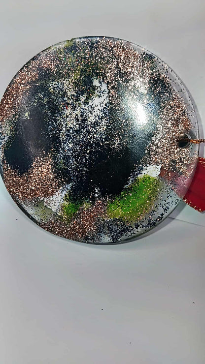 Round decorative item with metallic and green speckles on a white background