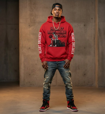 Person wearing a red hoodie with 'Heart Breaker Club' text and graphics, standing against a concrete wall.